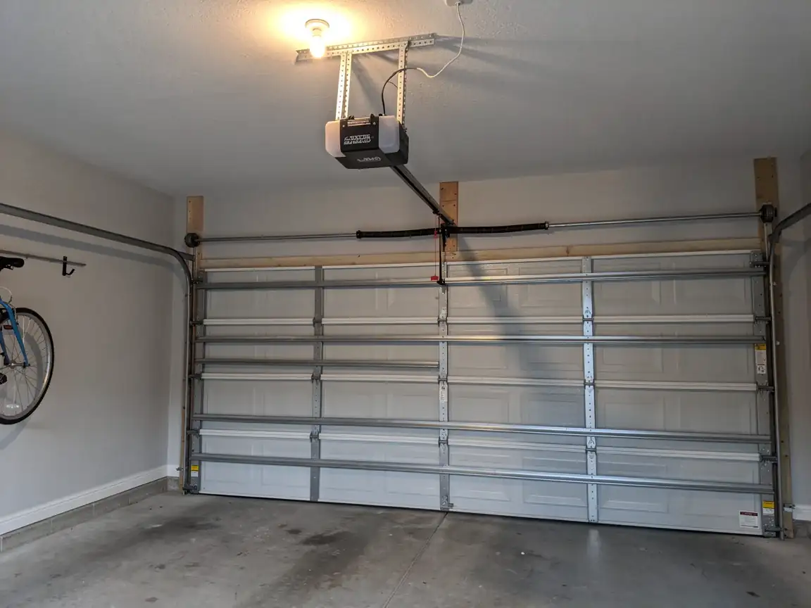 The garage door is closed, with an opener and torsion spring visible above.